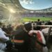 Paul und Svenja im Stadion, sie sind beide behindert, sitzen eng beieinander und verfolgen ein Fußballspiel, die Sonne scheint ins Stadion.