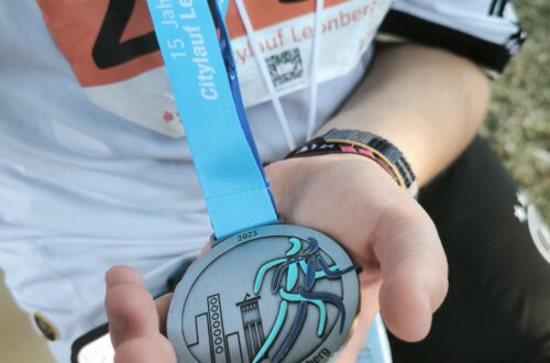 Nahaufnahme einer hellblauen Medaille des 15. Citylaufs Leonberg 2025, die von einer Person in einem Laufshirt mit Startnummer 2455 gehalten wird.
